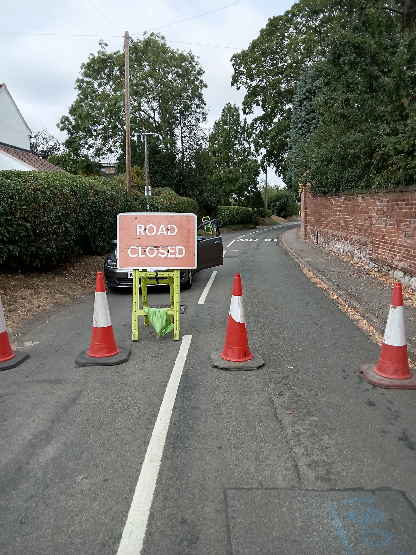 Road closed sign and cones set out for street works on a village road